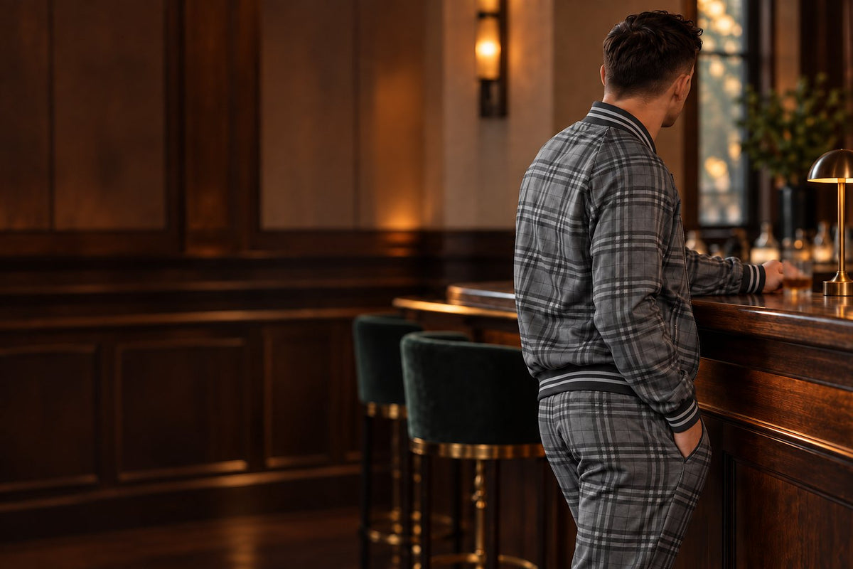 Man in a grey plaid Gentlemen tracksuit, bomber jacket and joggers, at a cocktail bar