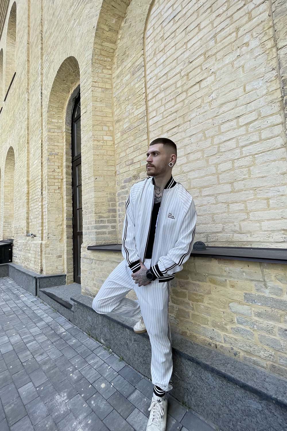 Premium White Pinstripe Colin Farrell Gentlemen Tracksuit — leaning against a wall