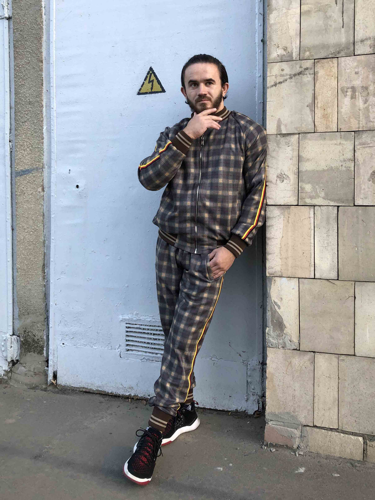 Brown Checkered Tracksuit — checkered bomber jacket and joggers inspired by The Gentlemen, leaning against a wall